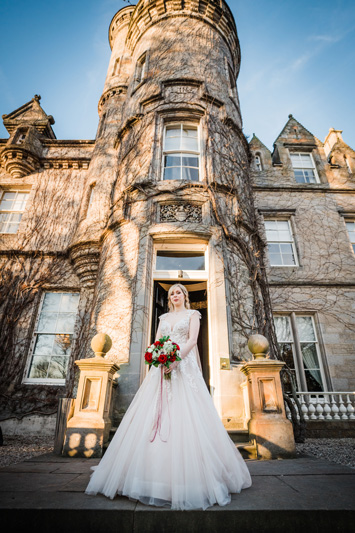 Bride in wedding dress and flowers standing outside Carlowrie Castle wedding