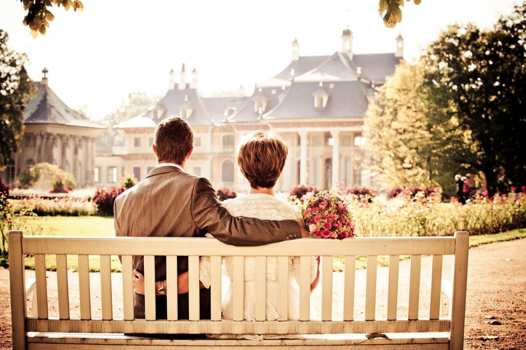 Couple sitting on bench looking at sunny wedding venue flowers
